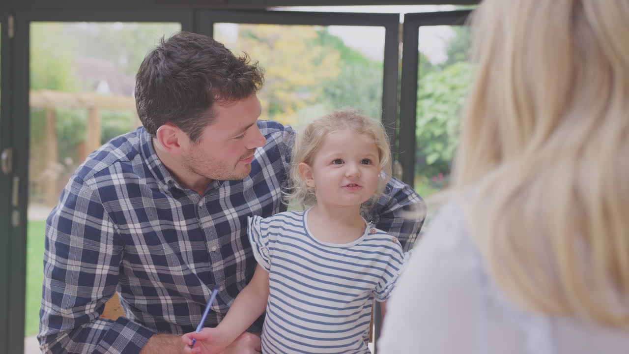 집에서 부 카운터에서 어린 딸이 책에 그림을 그리도록 돕는 부모 - 느린 동작으로 촬영