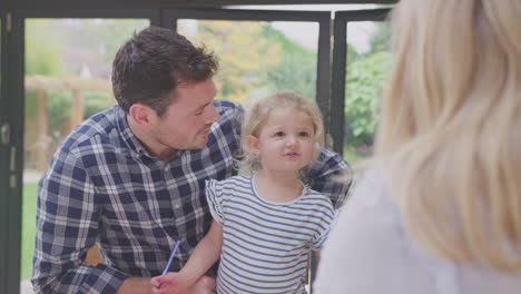 parents at home at kitchen counter helping young daughter to draw picture in book - shot in slow motion