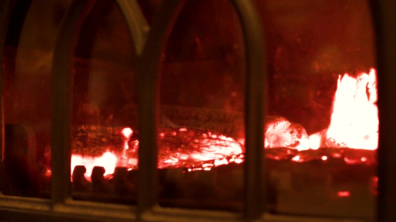 Close-up of bright orange flames and glowing embers burning inside a traditional cast iron fireplace.