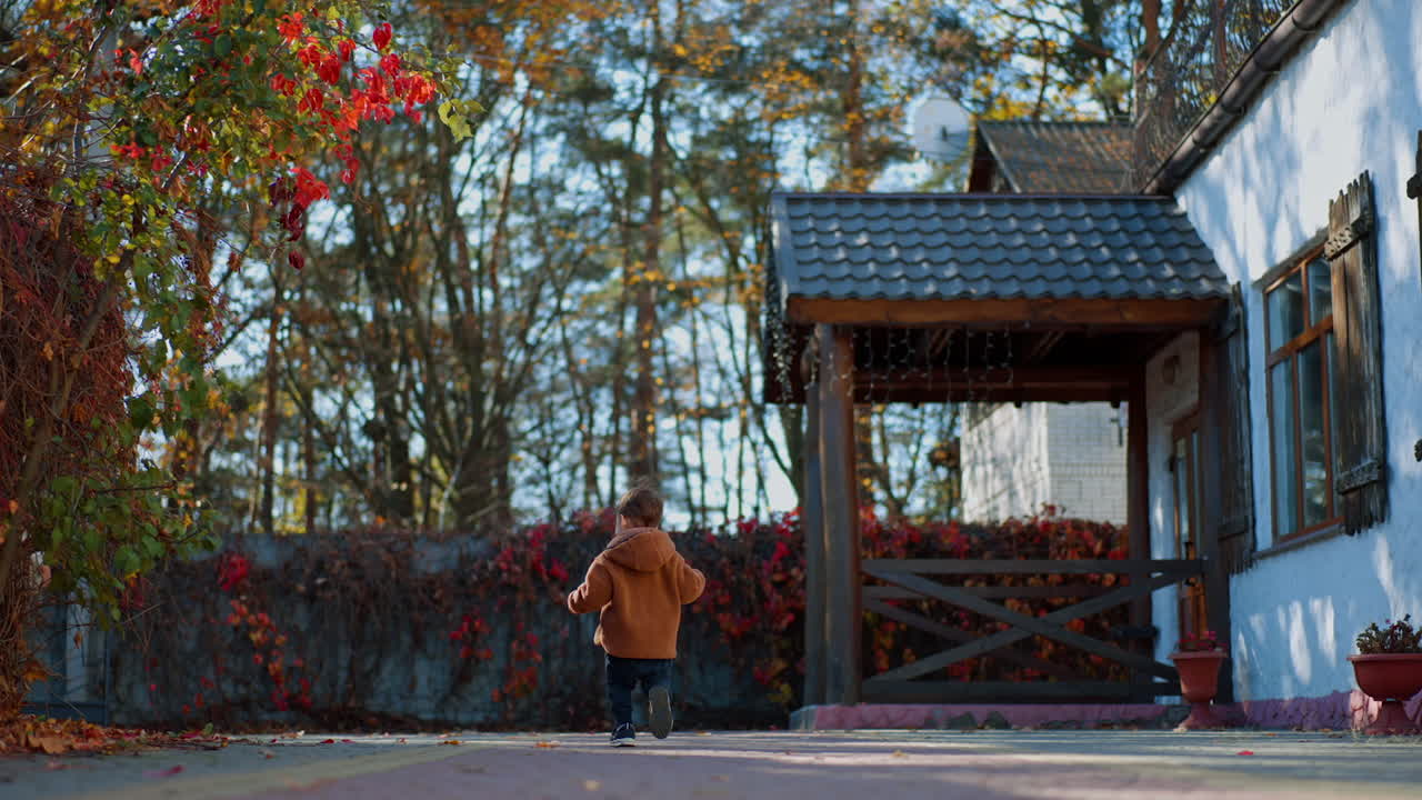 Rear view of a toddler running away from camera. Active time-spending outdoors in warm autumn season. Low angle view.