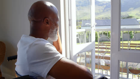 Side-view-of-mature-black-handicap-man-sitting-on-wheelchair-near-the-window-at-home-4k