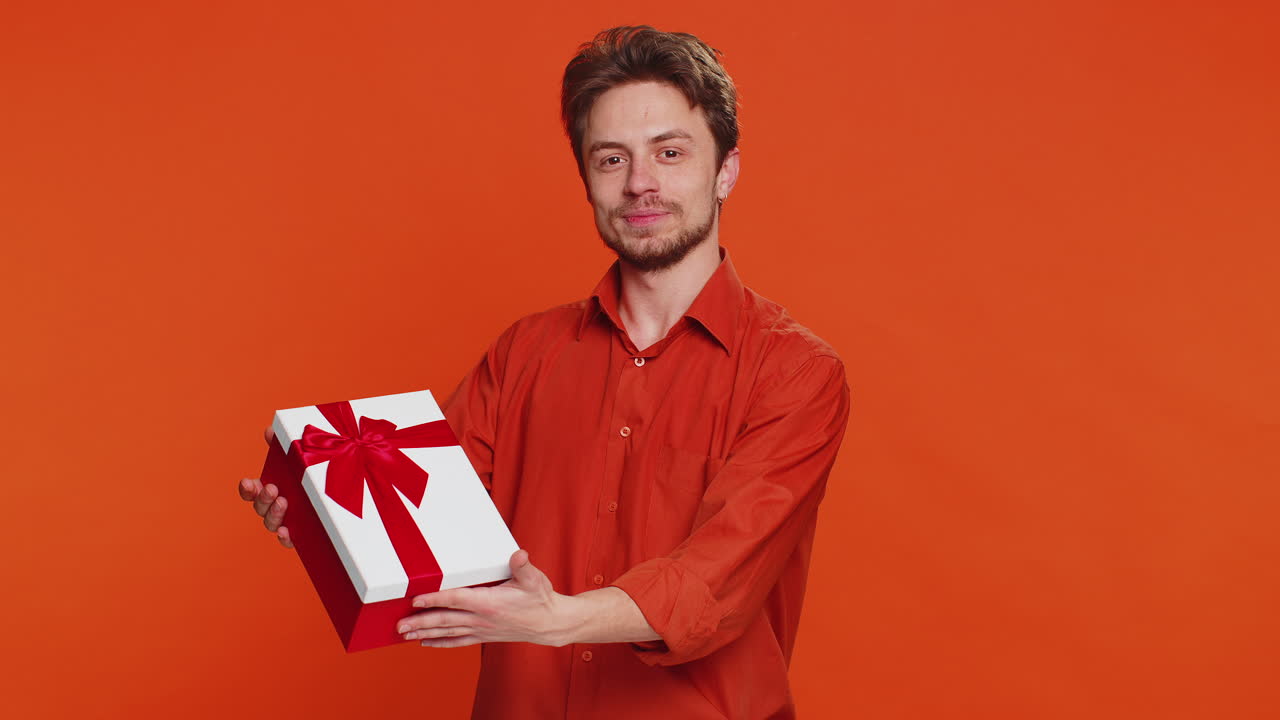 Smiling young man presenting birthday gift present box stretches out hands promotion discount sale