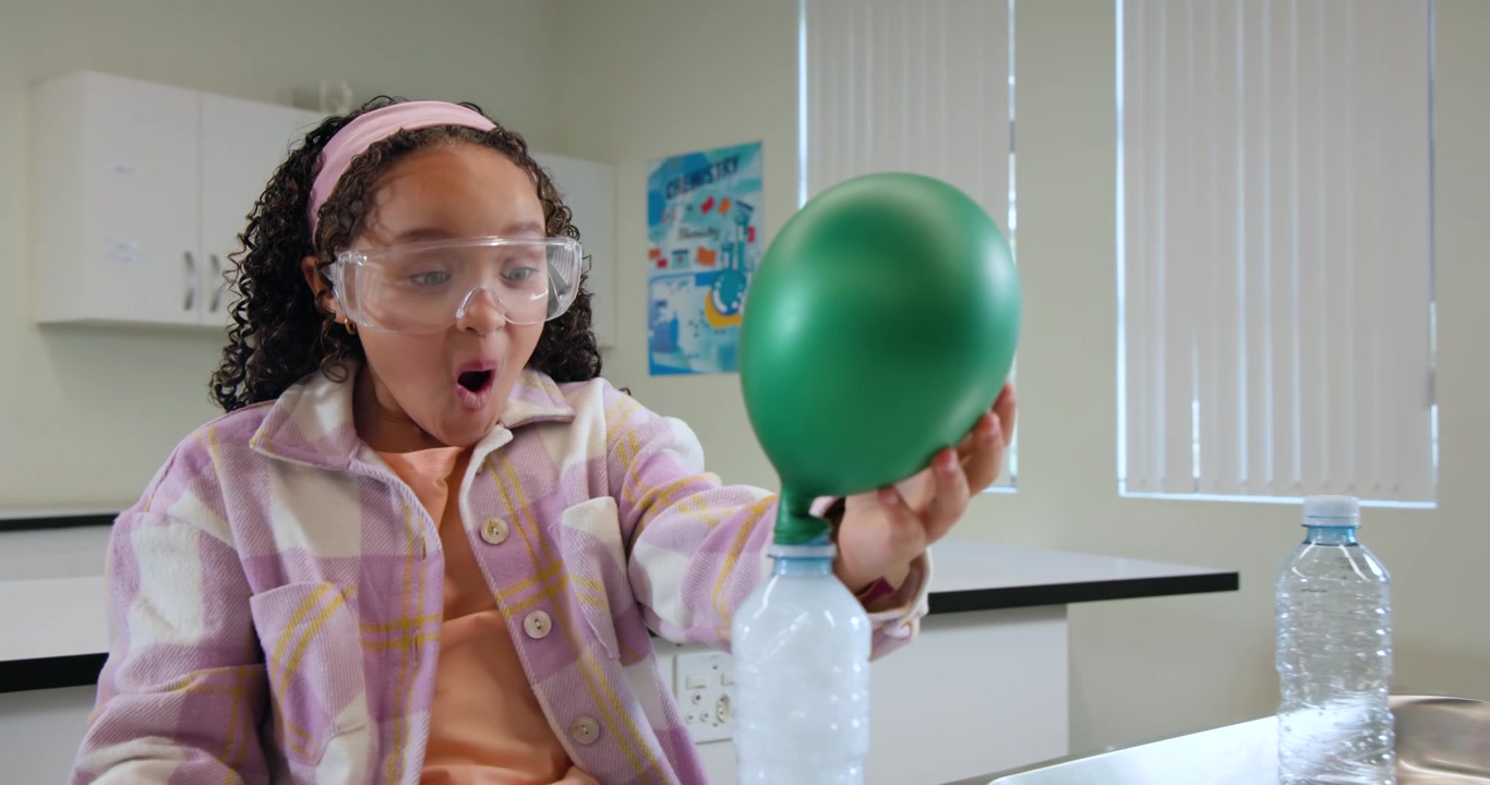 Bambino afroamericano che aggiunge una goccia con la pipetta in una bottiglia in laboratorio, osservando un palloncino verde che si gonfia.