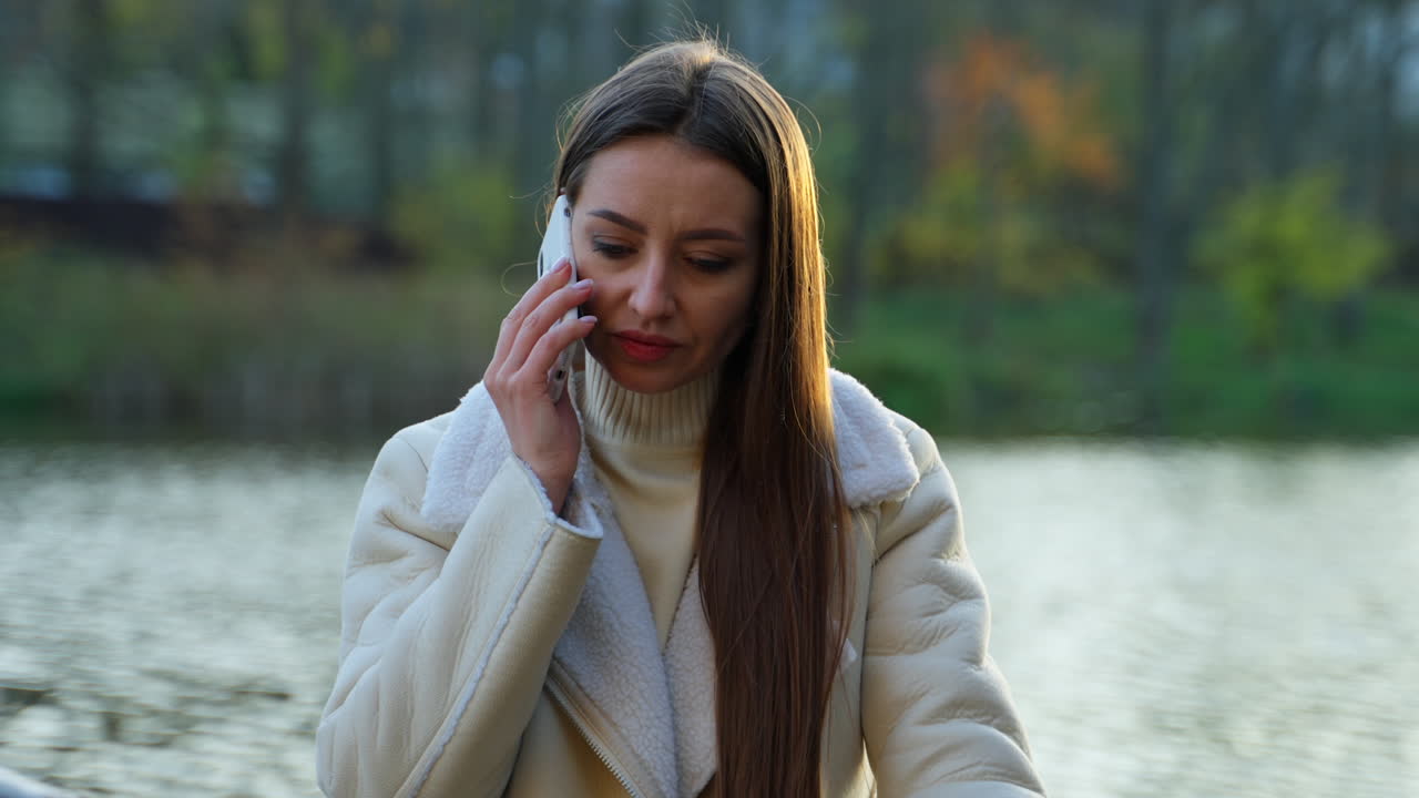 Woman talking on phone in a park near a lake