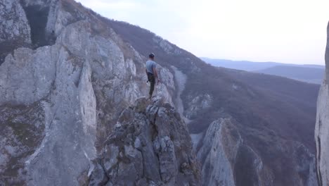 ascending aerial view of peaks in turda gorge, romania reveals climber on top on small rocky summit overlooking the incredible terrain and scenery of the mountains and ravine