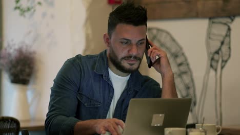 hombre barbudo trabajando con un teléfono inteligente y una computadora portátil en un café