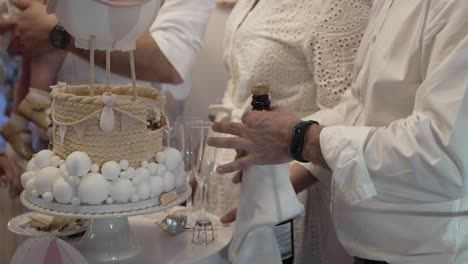 close-up of a decorative cake and a person opening a bottle at a baptism celebration