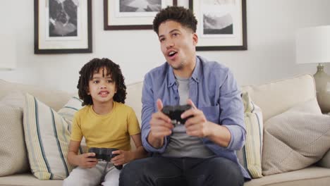 hombre biracial feliz y su hijo jugando videojuegos