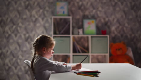 upset little girl draws picture with crayon sitting at table