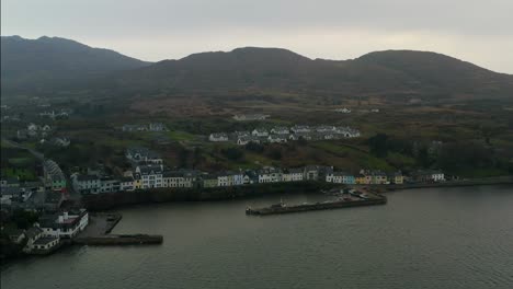 aerial-pan-of-Roundstone-harbour,-colourful-houses-and-Connemara-mountains-in-the-background