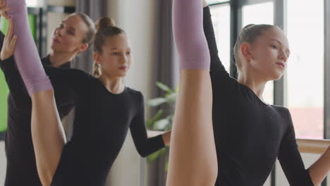 two gymnastic blonde girls rehearsing a ballet move in front of ballet barre