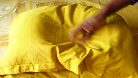 yellow pillow on a bed with a hand