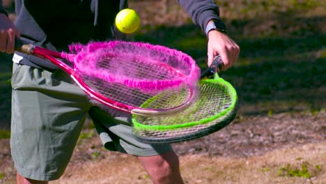 two tennis rackets covered in pink and green powder being hit by a tennis ball in slow motion during summer time