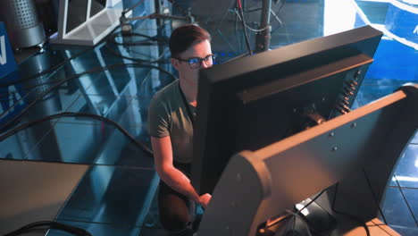 a person kneeling and adjusting a screen in a studio environment with visible cameras and lighting equipment. the focus is on the work being done with professional production gear in the background