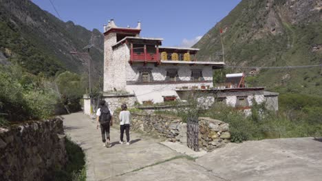 couple walks up driveway in traditional tibetan village in sichuan china with backpack