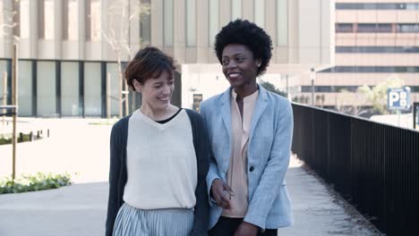 Front-view-of-two-cheerful-friends-walking-on-street-and-talking