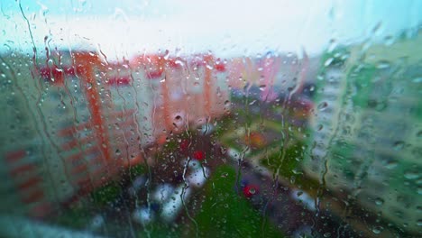 heavy rain outdoors. view from inside through the wet window on the city buildings. raindrops falling down on a glass window.