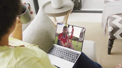 African-american-woman-using-laptop-with-diverse-male-soccer-players-playing-match-on-screen