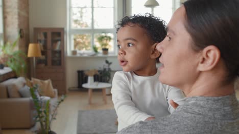 rear view of mother holding her baby in the living room while baby moves his arms and talks