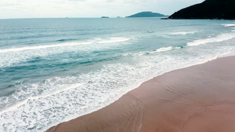 Un-Encantador-Avance-De-Un-Dron-Sobre-Praia-Brava,-Florianópolis,-Con-Olas,-Una-Montaña-Majestuosa-Y-El-Mar-Infinito-De-Fondo,-Capturando-El-Encanto-Costero