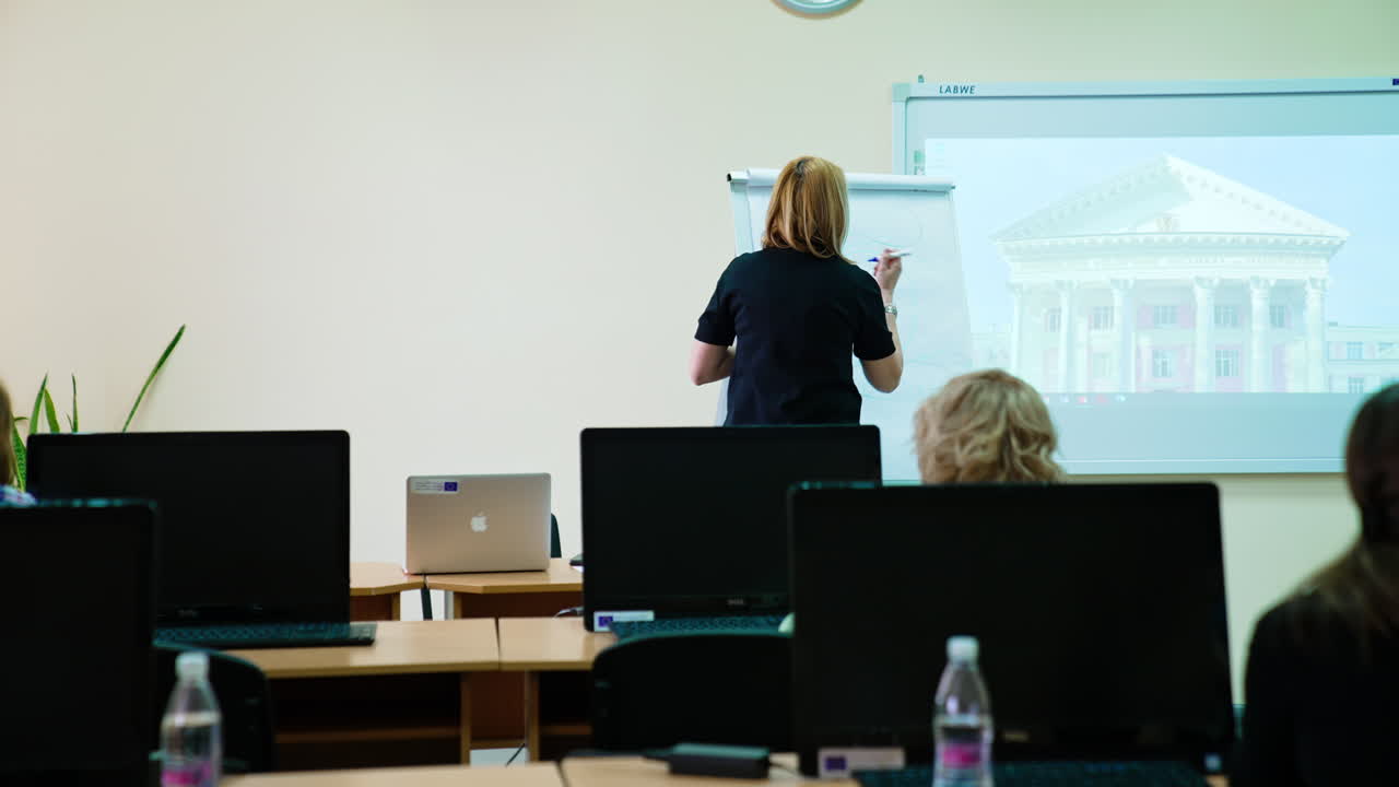 Students look at the lecturer drawing a scheme at the blackboard. Female teacher at mask explaining the eyeball structure.
