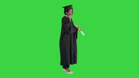 african american female student in graduation robe talking on the phone on a green screen, chroma key