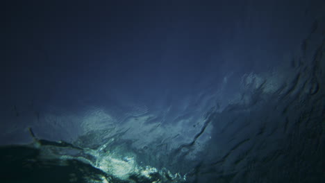 sun glistens as crashing ocean wave mist foam spreads on surface, underwater looking up
