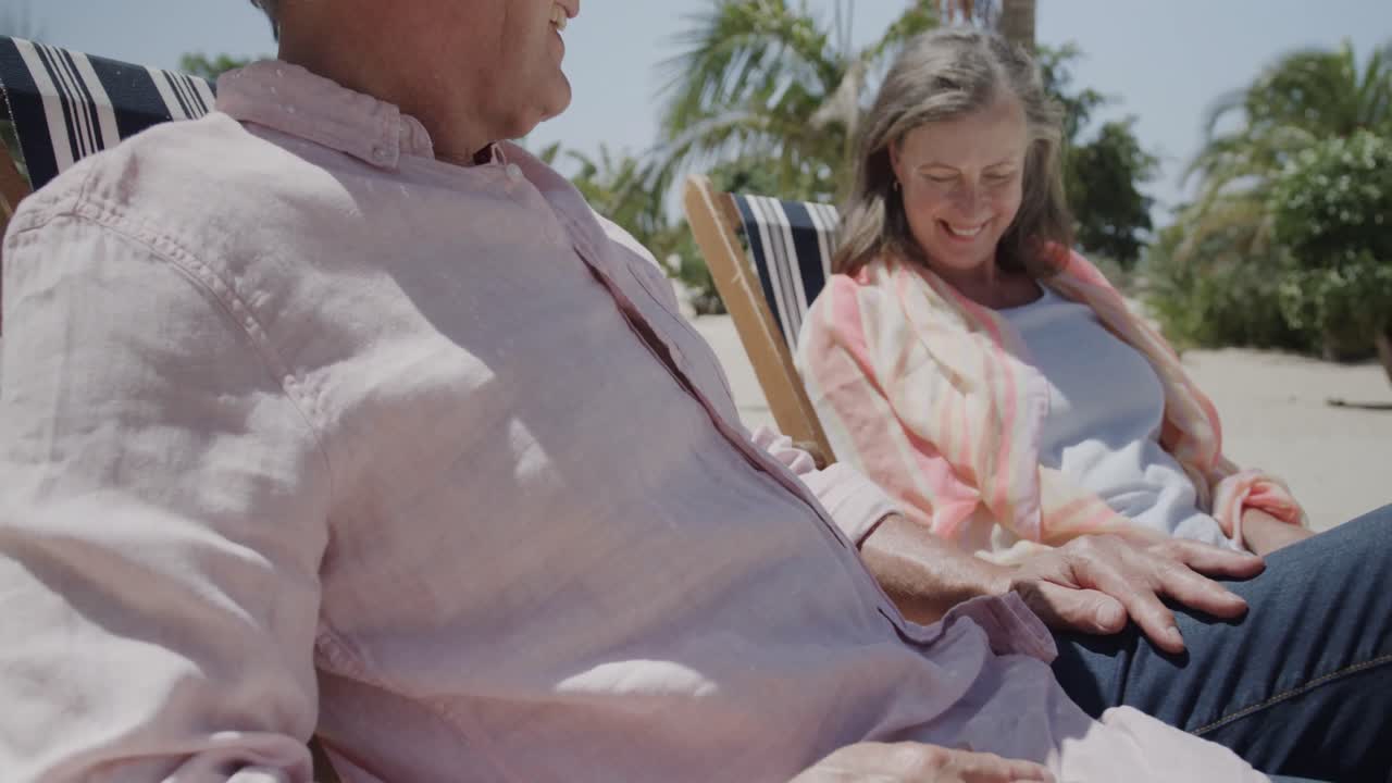 행복한 고위 백인 커플이 빛 해변에서 느린 동작으로 앉아서 대화를 나누고 있습니다.