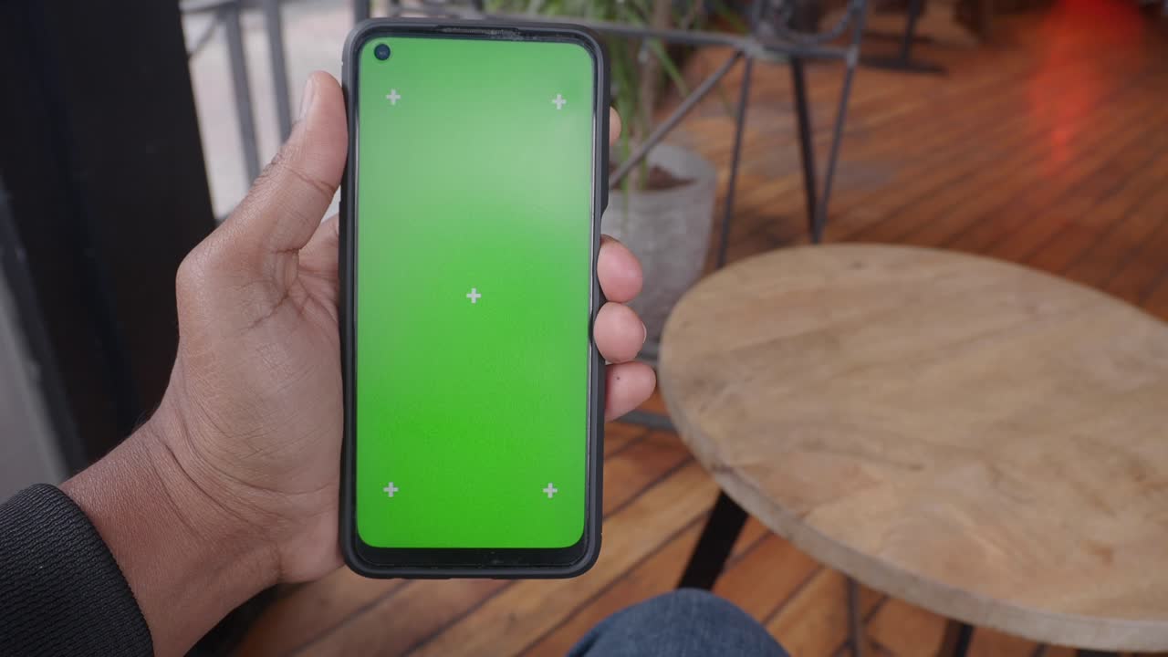 Person holding a smartphone with green screen in a cafe.