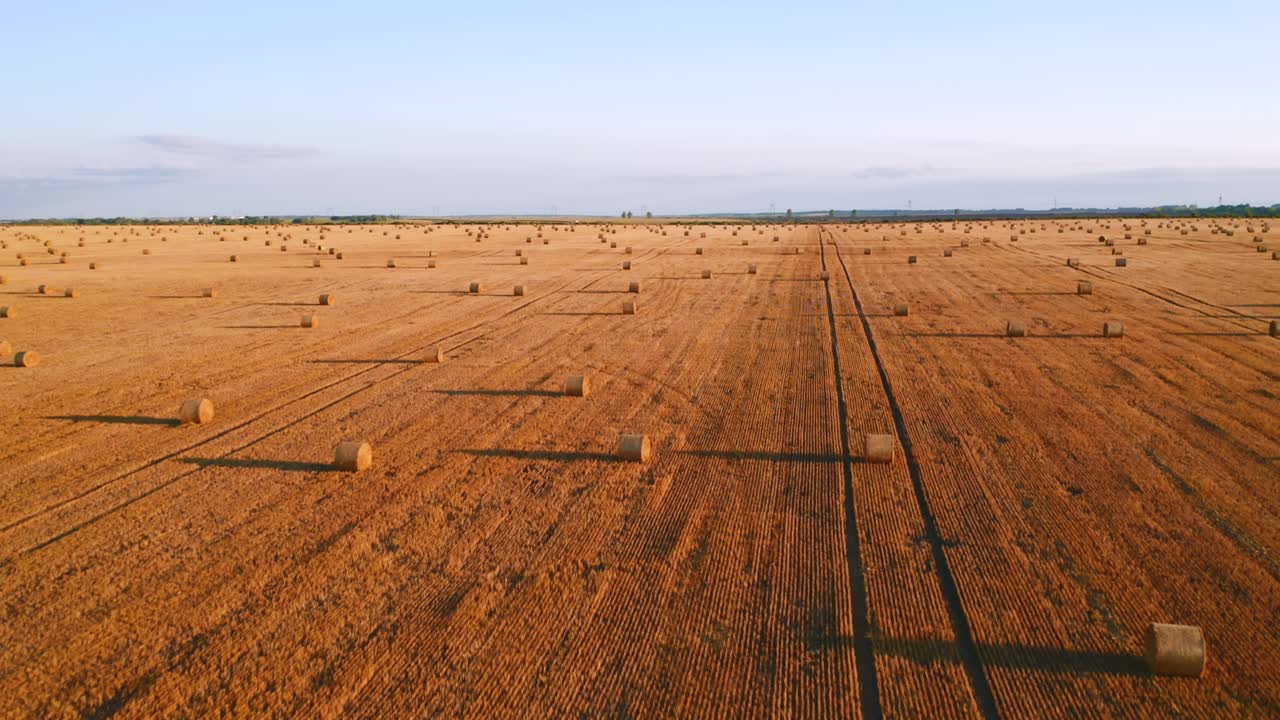 Drone flying above picturesque farmland with golden haystacks on a sunny day.