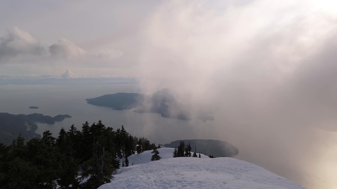Snowy mountaintop view of islands, ocean, clouds, and sunshine in BC, Canada.