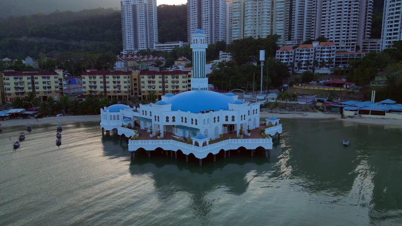 Mezquita flotante Tanjung Bungah en Penang, Malasia, situada sobre el mar con un vibrante paisaje urbano y barcos en la bahía. Hermosa vista aérea panorámica estática de dron