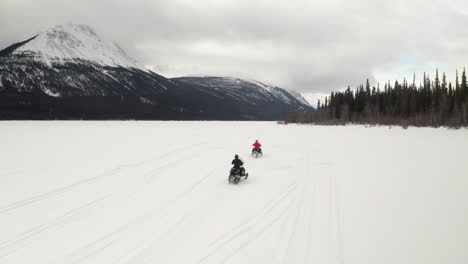 drone shot of two people snowmobiling on a frozen lake