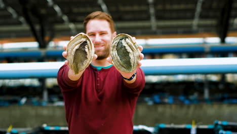 caucasian man on aquafarm holds out two farmed south african abalone, frontal