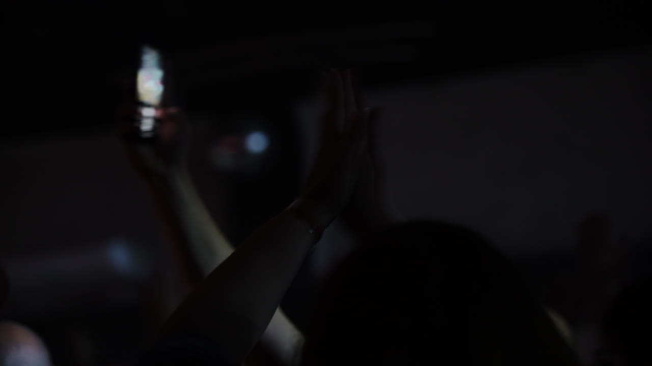 Energetic concert audience clapping, recording performance with smartphones, radiating enthusiasm and shared joy inside dimly lit music venue