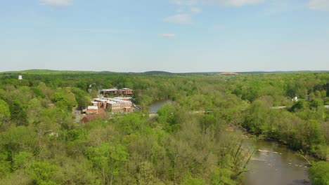 Drohnen-Luftaufstieg-über-Einem-Wald-Und-Einem-Fluss-Mit-Fabrik-Im-Hintergrund