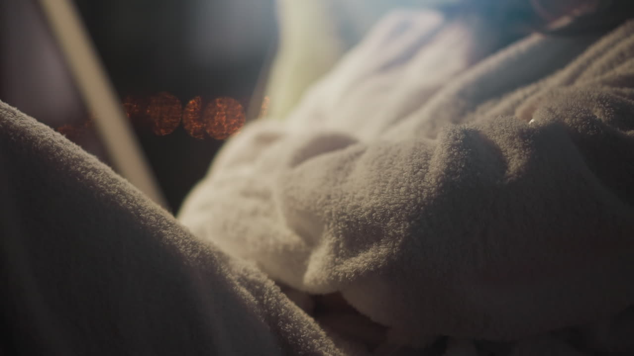 테리 목욕복을 입은 여성은 창문에 맞춰 의자에 앉아 야간 생활 환경을 바라보고 있습니다. 여자는 휴식을 취하고 아파트에서 느린 동작의 전망을 즐기고 있습니다.