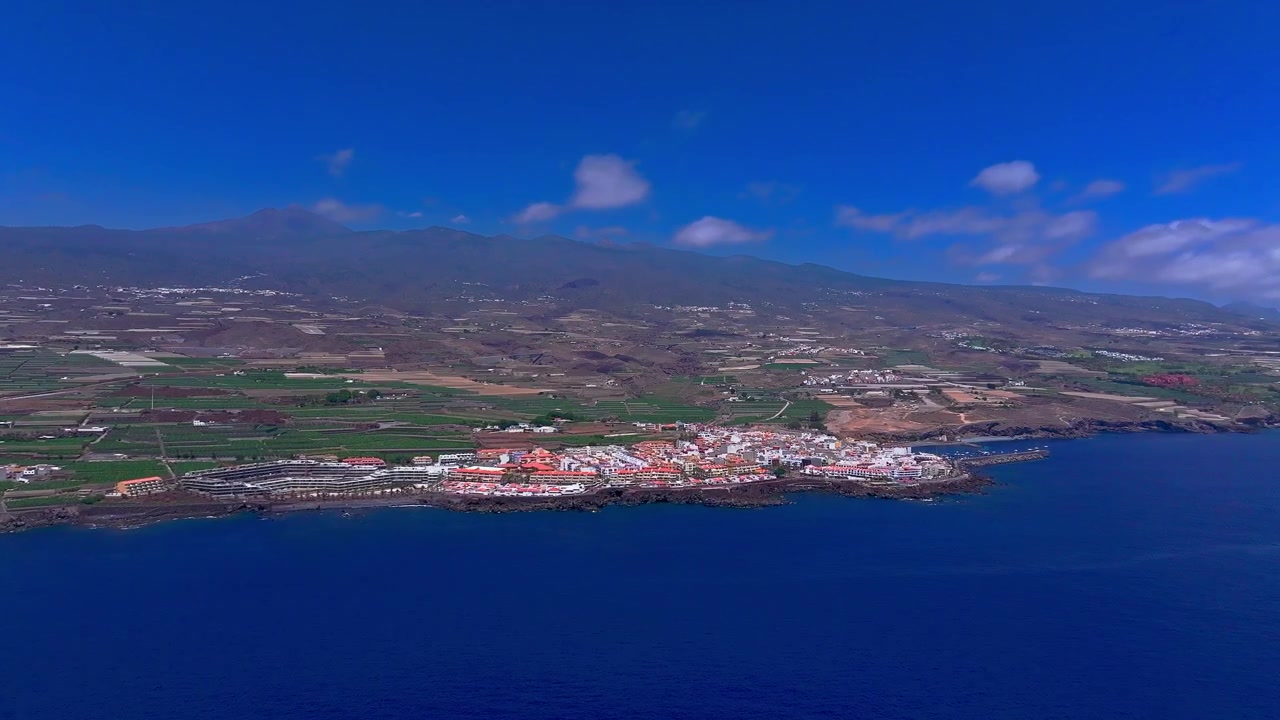 Vista aérea de un pueblo costero y tierras de cultivo que se encuentran con el Océano Atlántico bajo un cielo azul