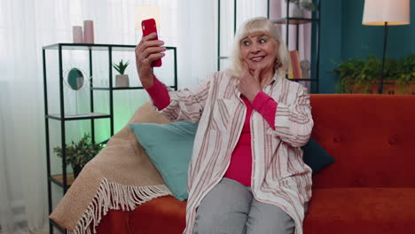 happy senior grandmother holding smartphone watching mobile video calling online making selfie home