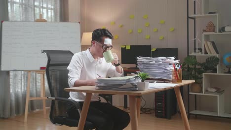 sick asian man drinking water while working hard with documents at the office