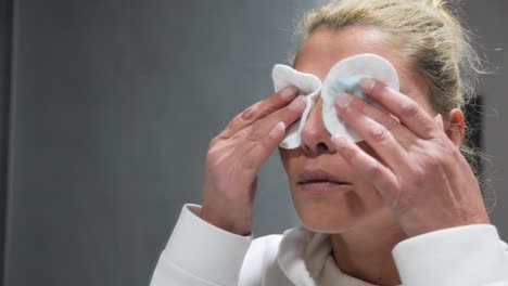 close-up of a woman's face as she is cleaning off her eye make-up with cotton cleansing pads