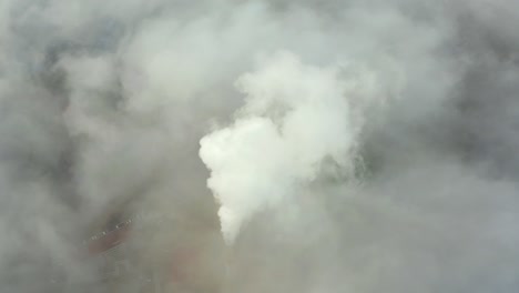 smoke from a power station chimney rising from a low, creeping fog. drone view