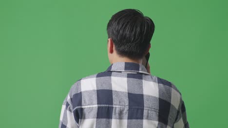 back view close up of asian man talking on mobile phone while walking on green screen in the studio