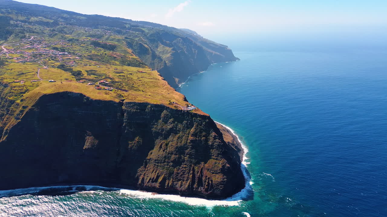 Inaccessible steep cliffs at the waterscape of the North Atlantic Ocean. Town located on the mount at the shore of the Madeira Islands, Portugal. Top view.