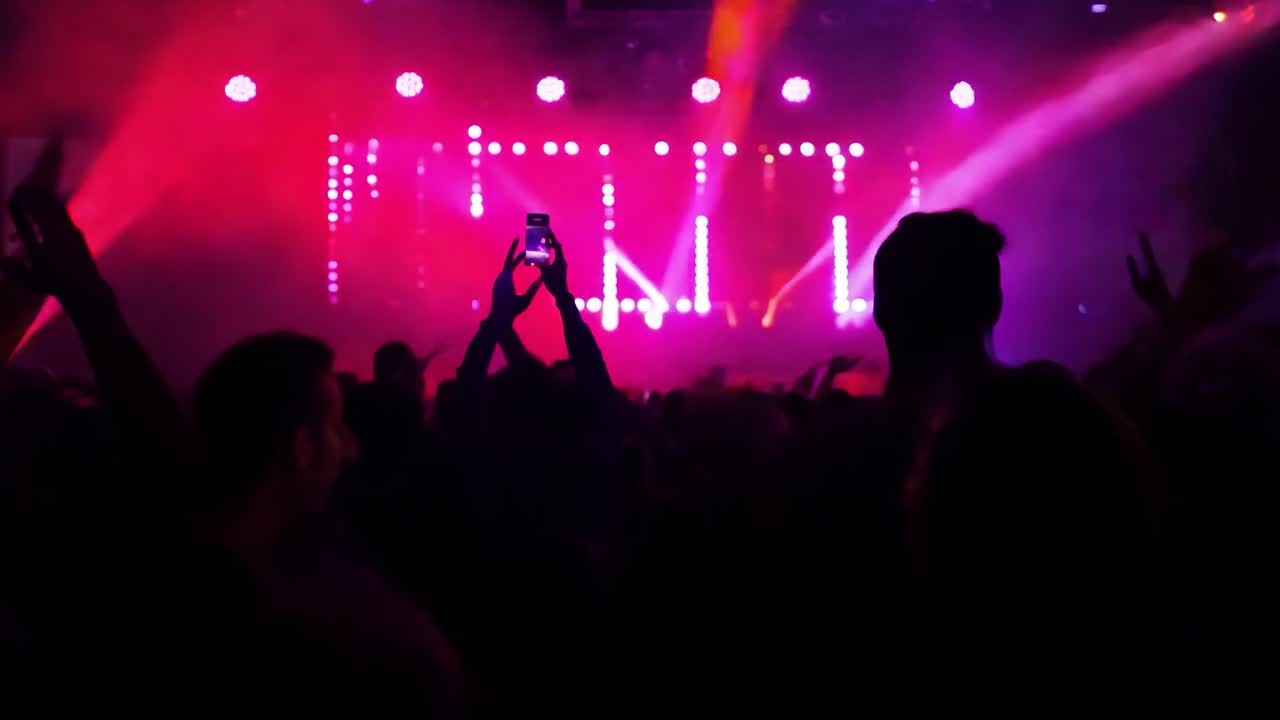 Folla a un concerto con mani alzate, luci del palco e silhouette