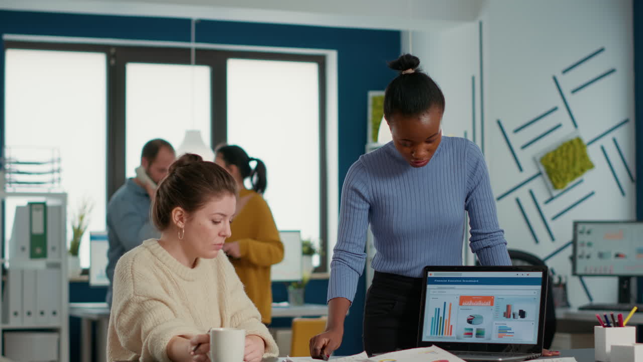African american startup employee presenting marketing strategy on laptop to coworker drinking cofee or tea