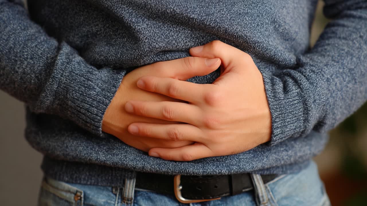 Una persona con malestar abdominal, sujetándose el estómago en una pose pensativa, mostrando signos de incomodidad mientras viste un cómodo suéter azul.