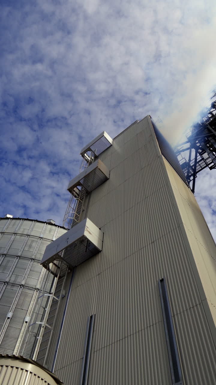 Modern warehouse. Grain elevator outdoors. Agricultural complex for grain processing. White fumes go from the industrial plant. View from below. Vertical video