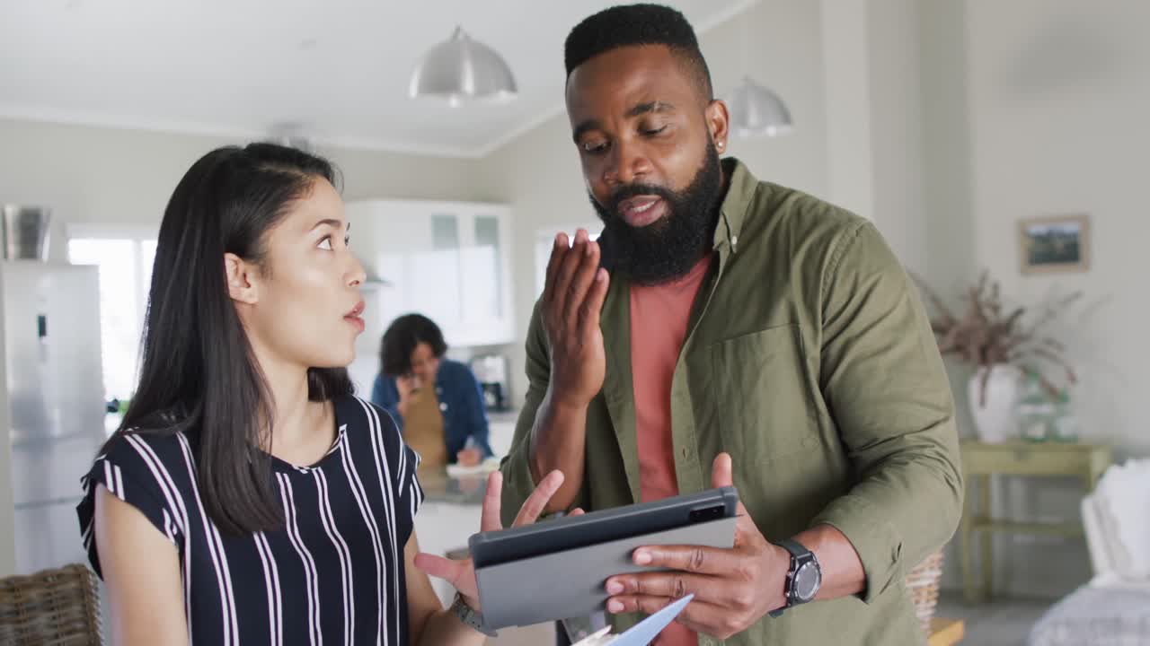 Happy diverse male and female friends talking, using tablet, working at home, in slow motion