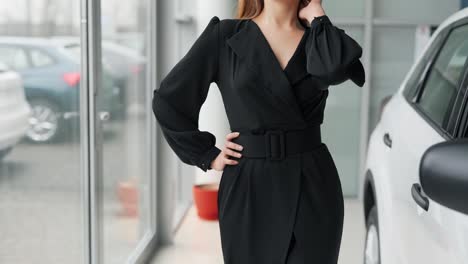 primer plano de una mujer vestida con un elegante vestido negro posando cerca de un coche